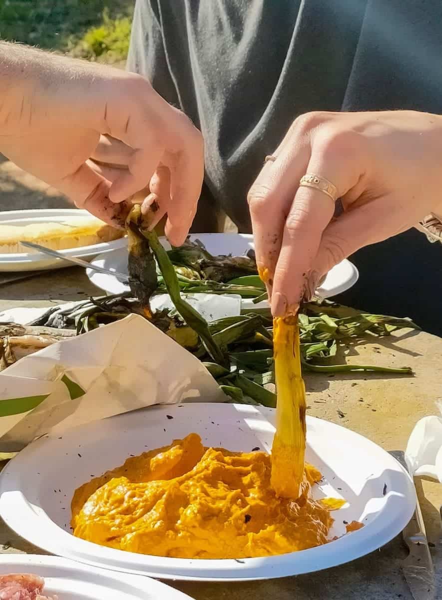 A person dipping a calçot in romesco sauce