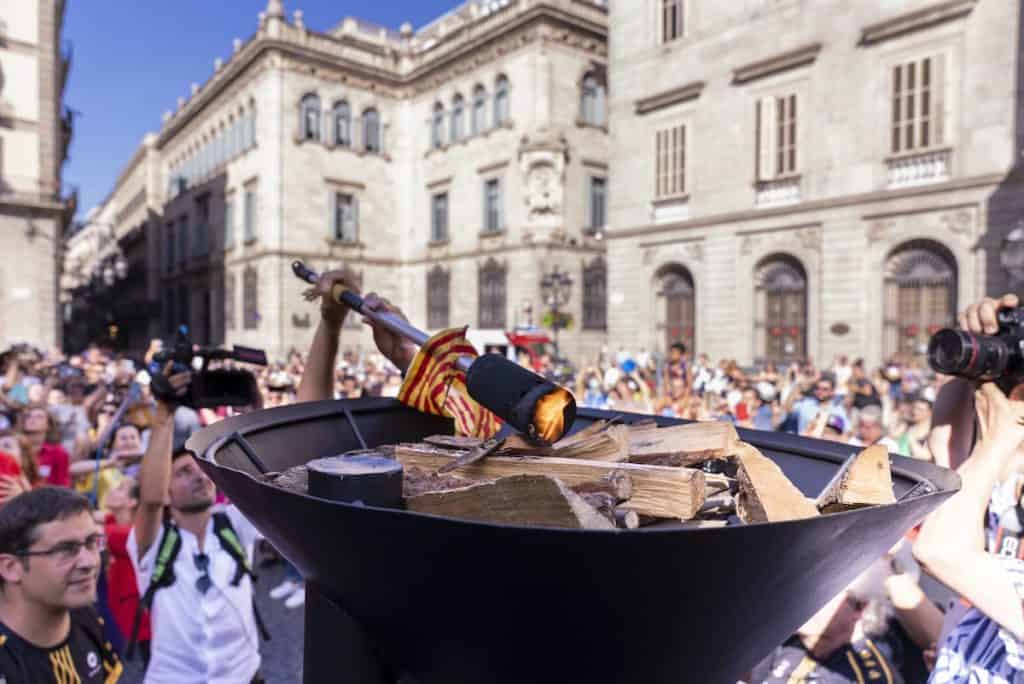 People lightning a fire with the Flama del Canigó in Plaça Sant Jaume (Barcelona)