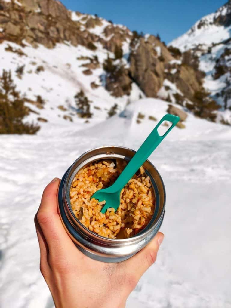 A person holding a lunch box of paella in the mountains